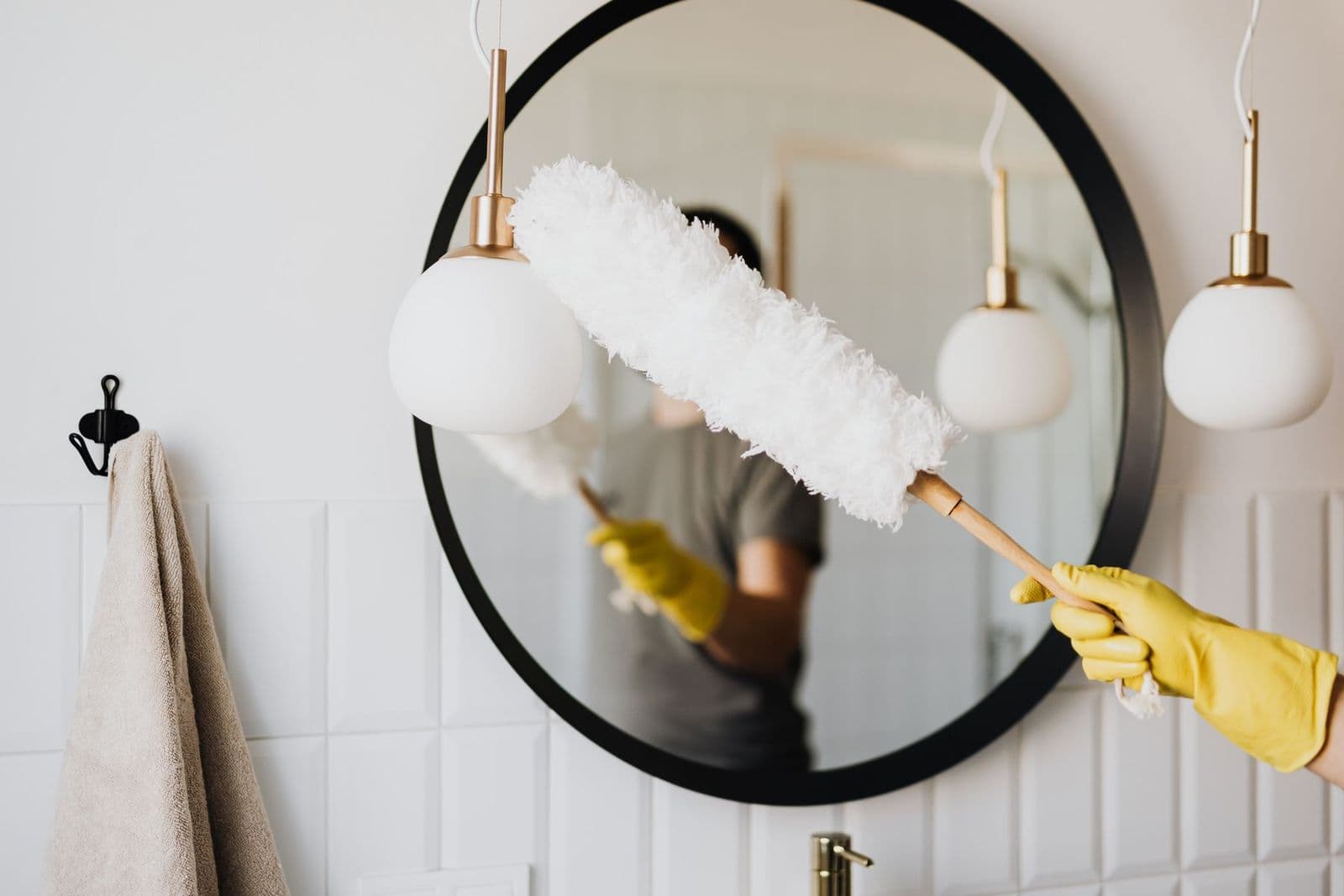 Gloved hand using a duster on a wall-mounted light fixture