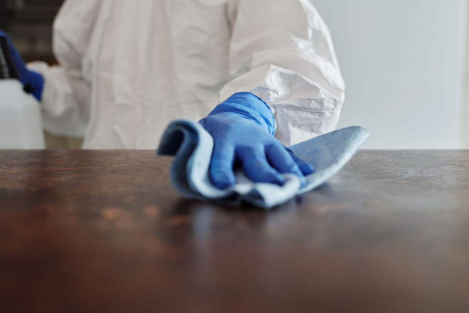 Gloved hand wiping down a work surface with a cleaning cloth
